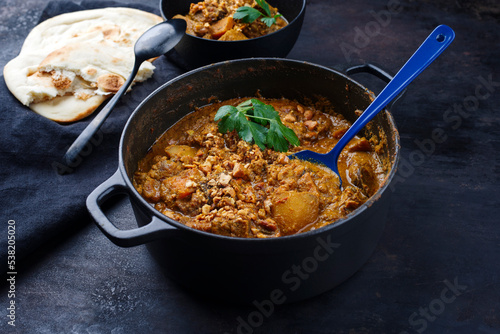Traditional Indian vegetarian Madras curry stew with sweet potatoes, roasted cashew nuts and garlic chapati bread served as close-up in saucepan