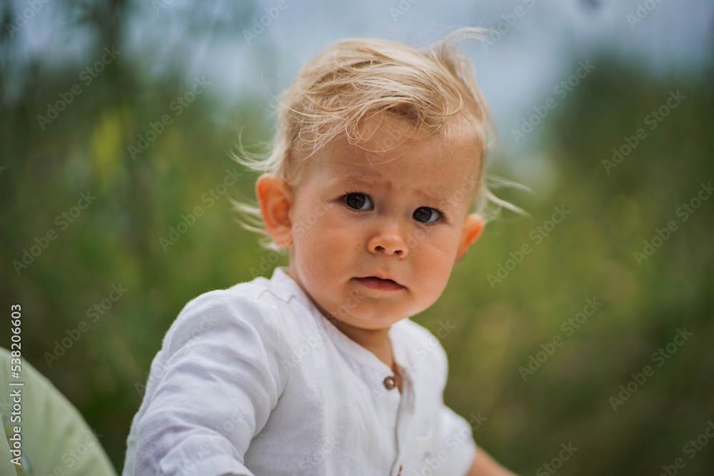 critical thoughtful one year old baby boy in chic festive summer clothes looking skeptical into the camera outdoor a idyllic & flowery garden with magical green grass in the background critical thoughtful one year old baby boy in chic festive summer clothes looking skeptical into the camera outdoor a idyllic & flowery garden with magical green grass in the background