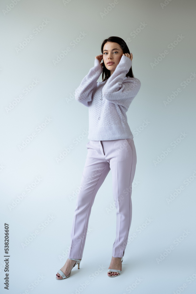 full length of young woman in sweater and pants fixing hair while posing on grey background. full length of young woman in sweater and pants fixing hair while posing on grey background.