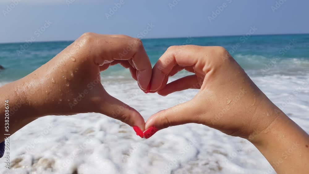 A young woman shows a heart shape with her hands while standing on the shore of the blue Mediterranean sea A young woman shows a heart shape with her hands while standing on the shore of the blue Mediterranean sea