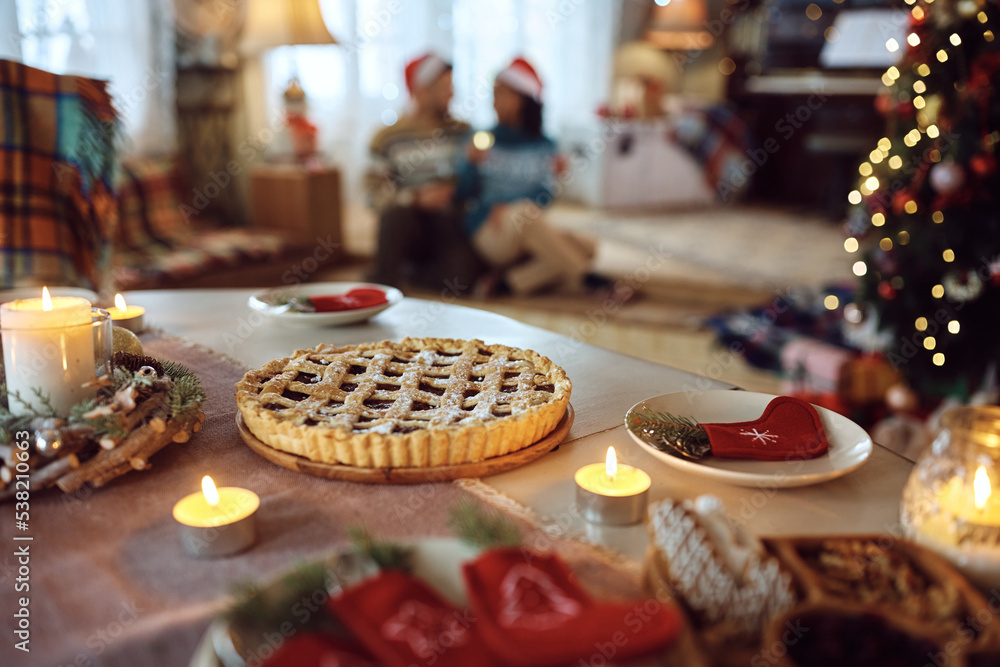 Christmas pie on decorated dining table with couple in background.