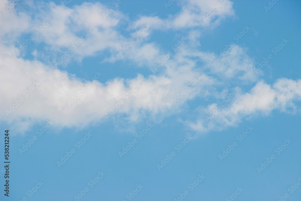 White fluffy clouds on a summer blue sky in cartoon style for background or wallpaper design. The background is white of round clouds in a blue sky. White fluffy clouds on a summer blue sky in cartoon style for background or wallpaper design. The background is white of round clouds in a blue sky.