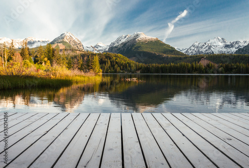 Mole (pier) on the lake in autumn scenery with beautiful and snowy mountains on background. Strbske pleso in High Tatras in fall with wooden mole and water reflection of landscape at sunrise. © Matt Benzero
