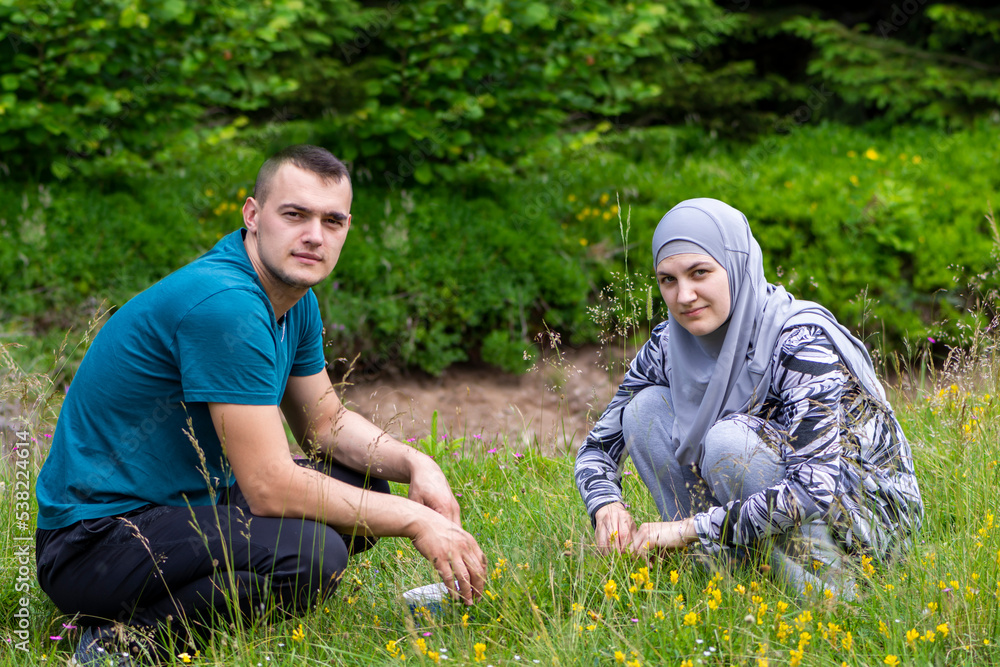 Young muslim couple squatting on grass and looking to the camera with different face expressions. Love, lifestyle and nature concept Young muslim couple squatting on grass and looking to the camera with different face expressions. Love, lifestyle and nature concept