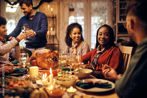 Happy black woman talks to friends during Thanksgiving meal at dining table.