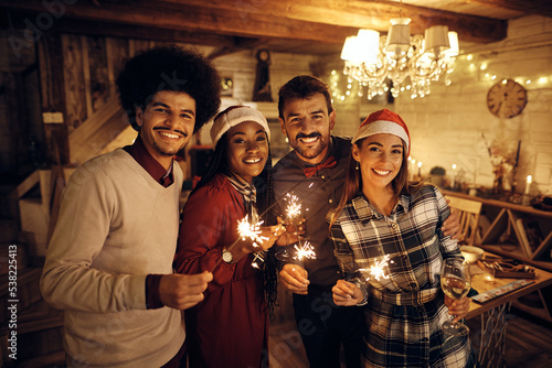 Young happy people using sparklers and drinking wine while celebrating New Year and looking at camera. photo