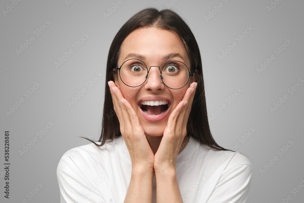 Young shocked female in round glasses shouting wow with open mouth isolated on gray Young shocked female in round glasses shouting wow with open mouth isolated on gray