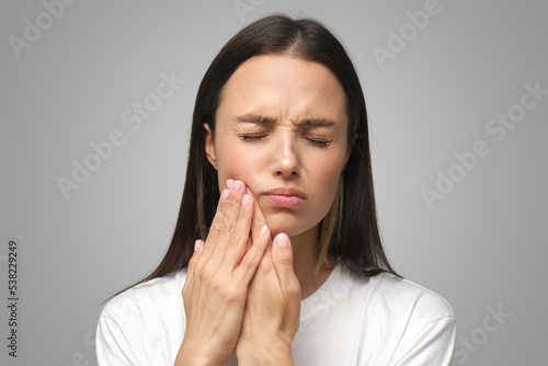 Miserable woman experiencing severe toothache, pressing palm to cheek, closing eyes because of pain photo