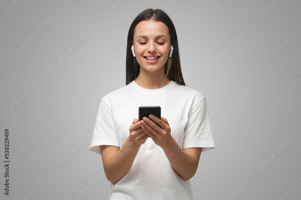 Pretty woman looking at smartphone, smiling on gray background Pretty woman looking at smartphone, smiling on gray background
