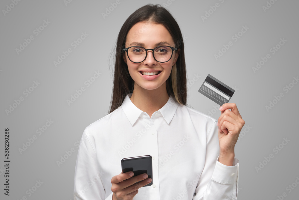 Young smiling woman holding credit card and phone on gray background Young smiling woman holding credit card and phone on gray background