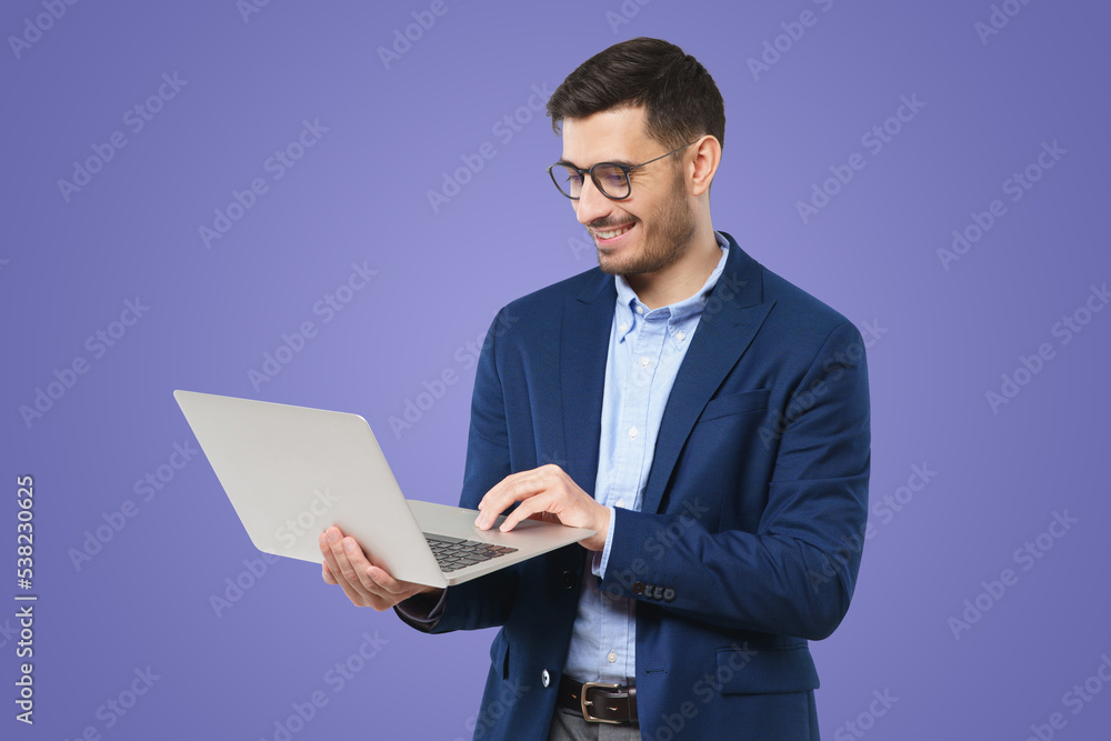 Modern businessman in blazer and shirt, standing with open laptop in hands, browsing websites