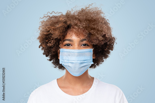 Smiling african american school girl with curly afro hair wearing medical mask and white t-shirt © Damir Khabirov