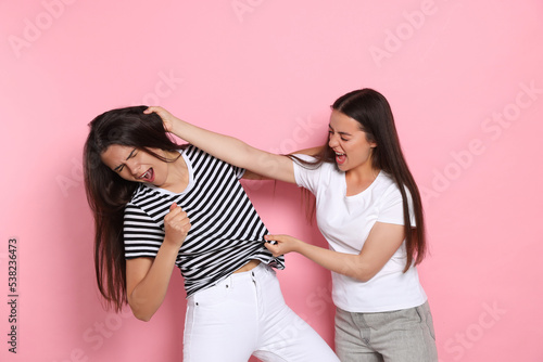 Aggressive young women fighting on pink background photo