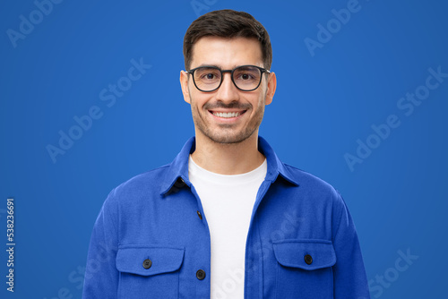 Close-up portrait of handsome smiling man wearing blue shirt and glasses, isolated on blue © Damir Khabirov