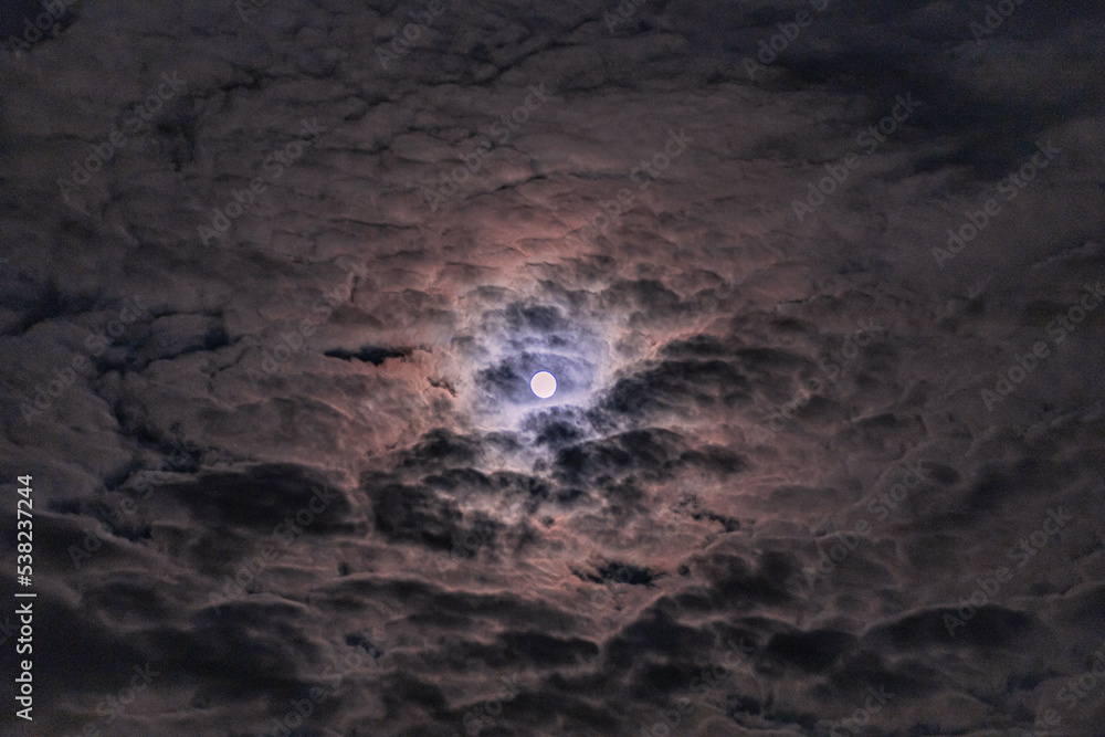 Bright full moon lighting up a cloudy night sky with glowing ring of light