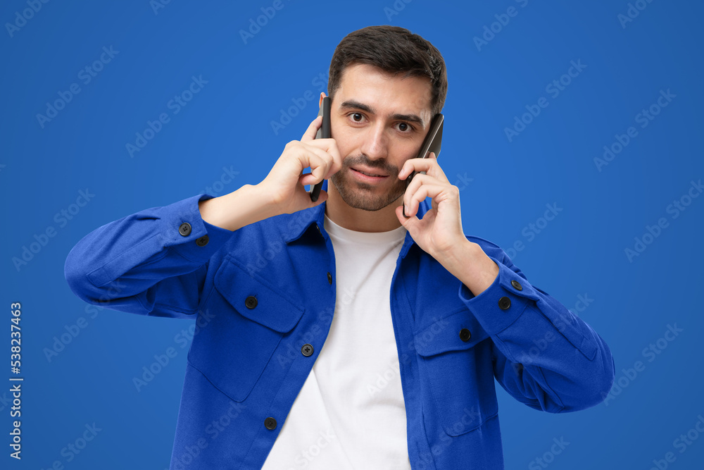 Overwhelmed business man talking on two phones, isolated on blue background Overwhelmed business man talking on two phones, isolated on blue background