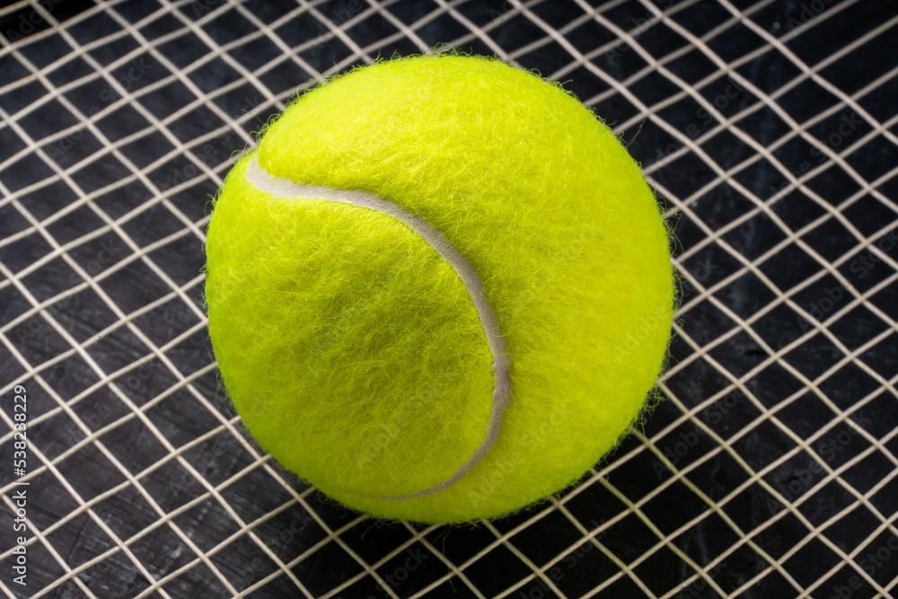 Tennis ball isolated on tennis racquet background, Yellow Tennis ball sports equipment on black background.