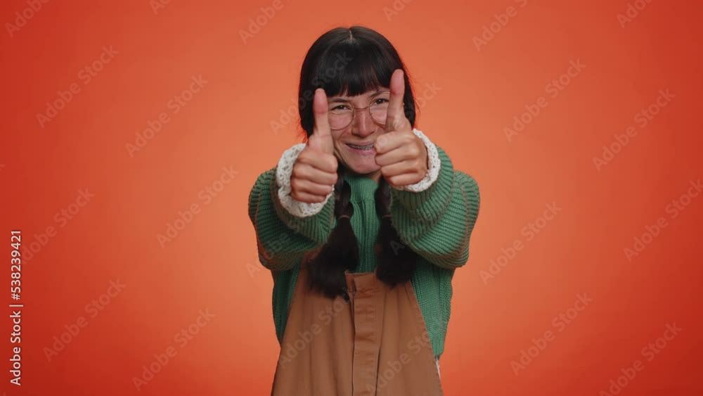 Like. Hipster nerd woman in green sweater raises thumbs up agrees with something or gives positive reply recommends advertisement likes good. Young girl isolated alone on orange studio background Like. Hipster nerd woman in green sweater raises thumbs up agrees with something or gives positive reply recommends advertisement likes good. Young girl isolated alone on orange studio background