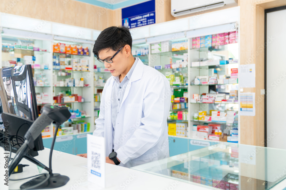 Medical pharmacy and healthcare providers concept. Handsome Asian man pharmacist working inspection medical product, drugs, medicine and supplements in package at cashier counter in modern drugstore.