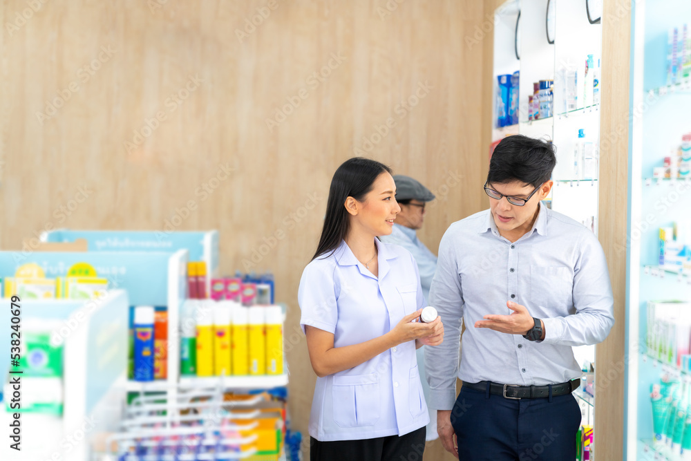 Attractive Asian woman pharmacist medication recommendation about medicine, drugs and supplements to male patient customer in modern drugstore. Medical pharmacy and healthcare providers concept. Attractive Asian woman pharmacist medication recommendation about medicine, drugs and supplements to male patient customer in modern drugstore. Medical pharmacy and healthcare providers concept.