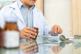 Medical pharmacy and healthcare providers concept. Asian man professional pharmacist counting drug pills on counting trays by hospital prescriptions on counter to patient customer in modern pharmacy.