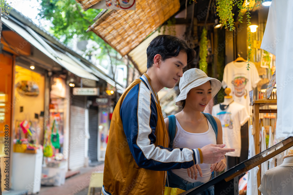 Young Asian couple enjoy and fun outdoor lifestyle shopping together at street market on summer holiday vacation. Happy man and woman choosing and buying fashion clothes together at clothing shop. Young Asian couple enjoy and fun outdoor lifestyle shopping together at street market on summer holiday vacation. Happy man and woman choosing and buying fashion clothes together at clothing shop.