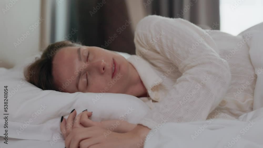 Sleepy woman waking up, turning on the pillow, smiling and stretching on the bed Sleepy woman waking up, turning on the pillow, smiling and stretching on the bed