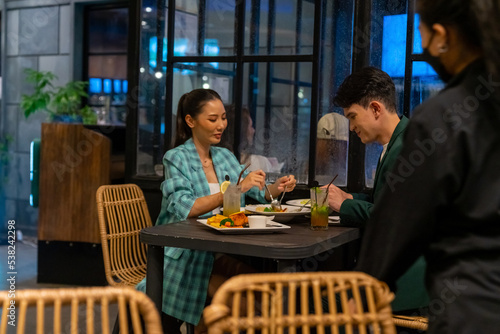 Asian couple celebrating holiday event at luxury restaurant bar in the city at night. Attractive man and woman enjoy city lifestyle shopping and having dinner with food and drink on travel vacation