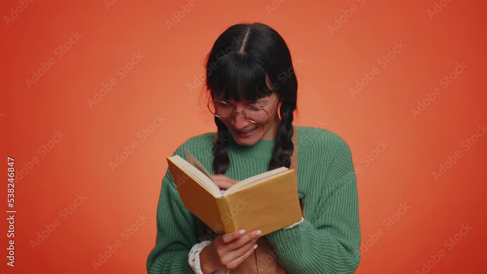 Young nerd woman with pigtails in glasses reading funny interesting fairytale story book, leisure hobby, knowledge wisdom, education, learning, study, wow. Latin girl isolated on orange background Young nerd woman with pigtails in glasses reading funny interesting fairytale story book, leisure hobby, knowledge wisdom, education, learning, study, wow. Latin girl isolated on orange background