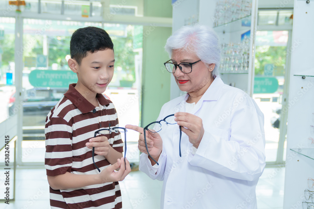 Middle-aged ophthalmologist examining young boy and giving eye consultation to Asian boy