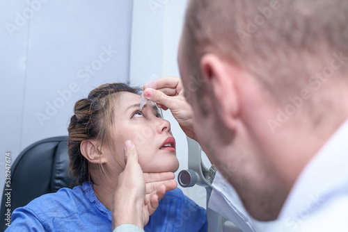 Male doctor ophthalmologists dripping eye drops on eyes of a female patient during a treatment at the ophthalmological office