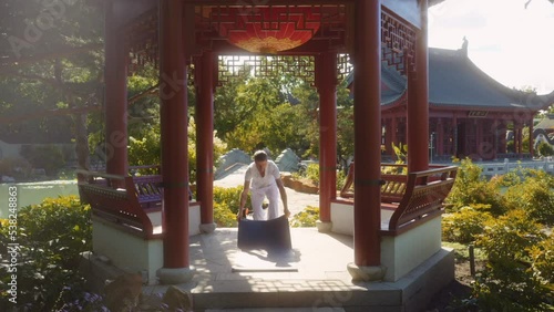 Caucasian adult male practices yoga. Surrounding ambience is that of a traditional Chinese temple with garden, pagoda, etc.

Putting down yoga mat and stepping on, nice flare, centred composition. photo