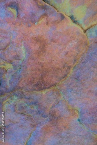 Close-up on psychedelic abstract rock texture and background or backdrop copy-space with predominantly purple, pink and red pastel colors and some hints of green lichen