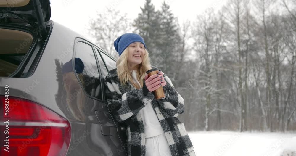 Young woman with hot drink near car at winter forest Young woman with hot drink near car at winter forest