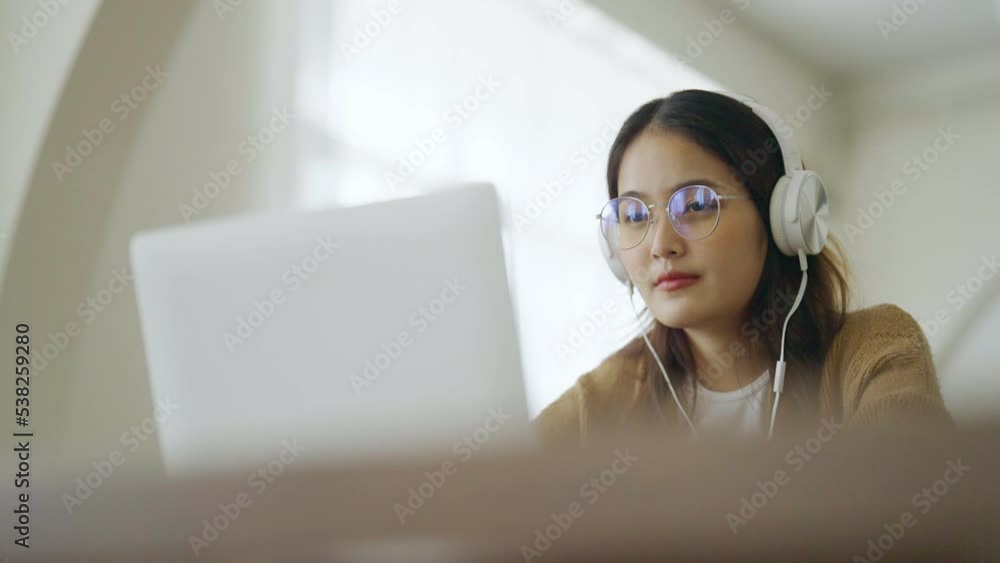 Young asian woman wearing glasses and headset working on computer laptop at house. Work at home, Video conference, Video call, Student learning online class Young asian woman wearing glasses and headset working on computer laptop at house. Work at home, Video conference, Video call, Student learning online class