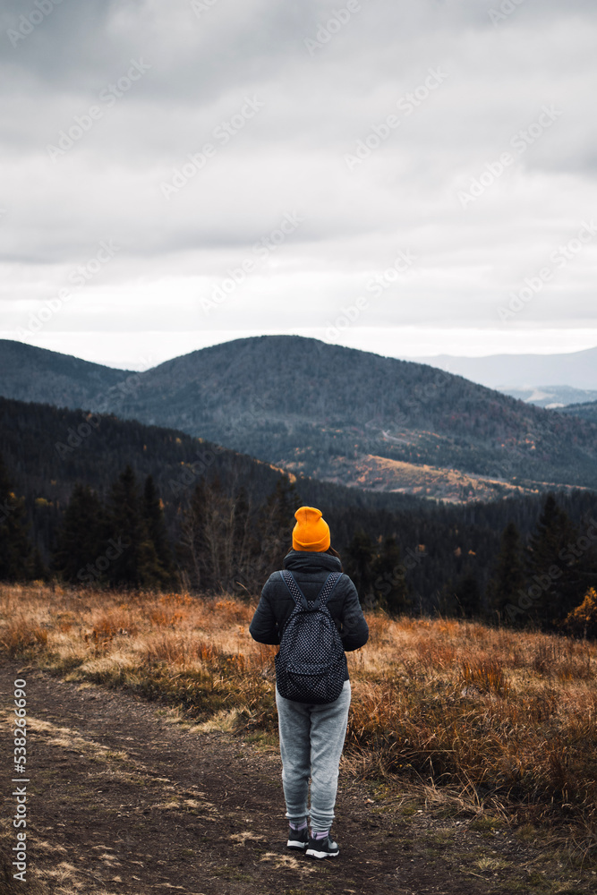 Young woman from behind is standing on the road to mountains and looking away Young woman from behind is standing on the road to mountains and looking away