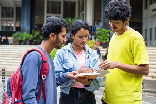 group of young indian Students busy on by discussing of syllabus during examination at college campus - concept of learning discussion and friendship.