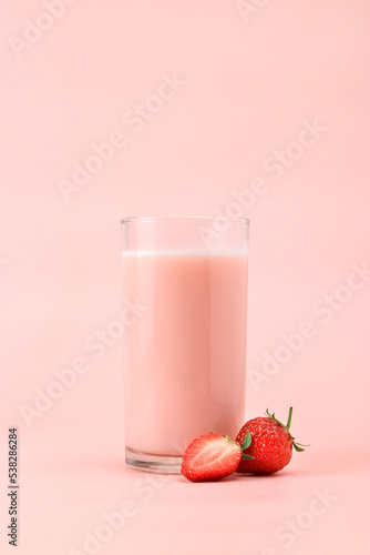 Glass with tasty strawberry smoothie / strawberry milk on pink background.
