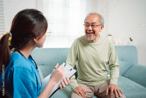 Asian caregiver talking senior male patient checkup in living room at home. Older elderly man consults after physical therapy. Nurse assistance rescue concept.