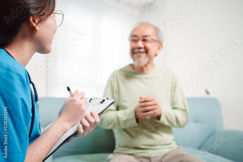 Asian caregiver talking senior male patient checkup in living room at home. Older elderly man consults after physical therapy. Nurse assistance rescue concept.