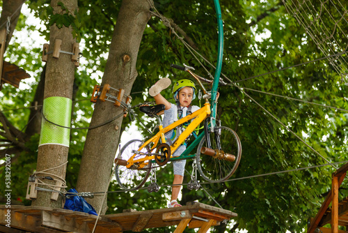 Little girl is standing on a rope, holding a rope with his hands. A child in a rope park passes obstacles