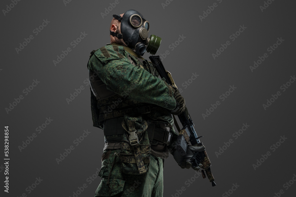Studio shot of russian soldier dressed in protective uniform and gas mask against gray background.