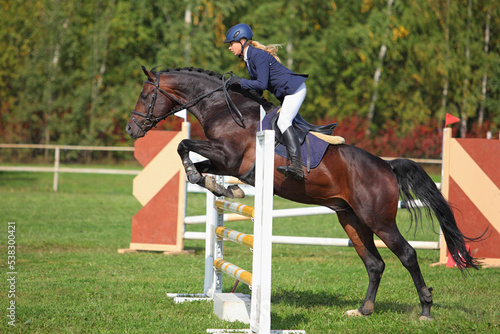 Young equestrian girl jumping obstacle with sports horse 