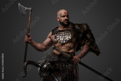 Shot of assaulting viking with muscular build and fur holding two axes.
