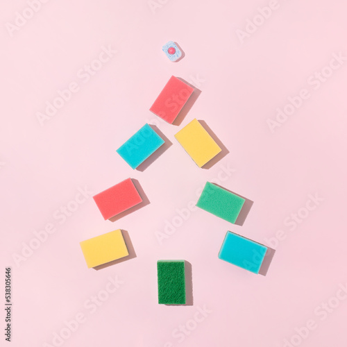 Clolorful cleaning sponges and dishwasher tablet on bright pink background. Minimal Christmas tree shape composition. Trendy Christmas or New Year party cleaning concept. photo