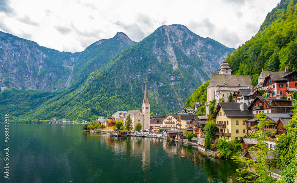 Famous view of Hallstatt city and church near the lake. Mountains in the background. Summer rainy day, soft colors, cloudy weather. Famous view of Hallstatt city and church near the lake. Mountains in the background. Summer rainy day, soft colors, cloudy weather.