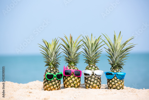 Tropical summer vacation family holiday, Pineapples wearing stylish sunglasses on the sand beach with sea background, Sunny day on the beach tropical island, summer tropical pineapple.