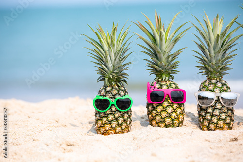 Tropical summer vacation family holiday, Pineapples wearing stylish sunglasses on the sand beach with sea background, Sunny day on the beach tropical island, summer tropical pineapple.