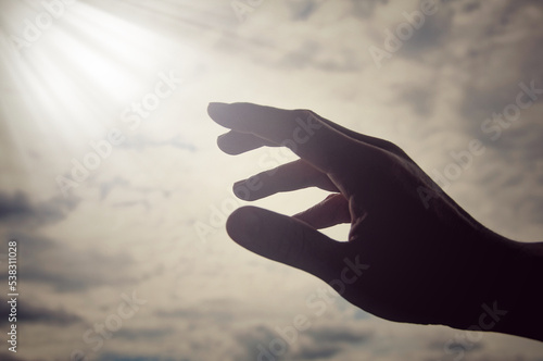 Hand reaching out to bright shining light on sky above. Religious and spiritual concept