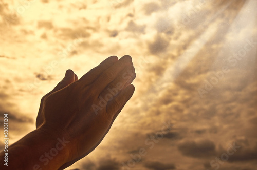 Hand praying with bright shining light on sky background. Religious and spiritual concept